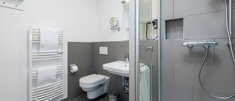 Un baño moderno con cabina de ducha de vidrio, inodoro blanco, lavamanos y toallero.