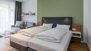 Een moderne hotelkamer met twee bedden, een bank, een klein tafeltje en een groene accentmuur.
