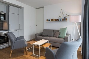 Una sala de estar moderna con sofás grises, una mesa de centro y una cocina con horno y microondas integrados.