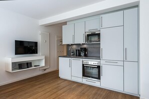 Una cocina compacta con armarios blancos, horno integrado, microondas y cafetera.