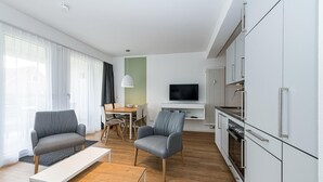 A modern living room with a dining area, a kitchen with white cabinets, and a flat-screen TV mounted on the wall. - Apartment nah der See mit Großer Terrasse, Parkplatz, Schwimmbad- & Saunanutzung (Nordseeheilbad Bensersiel)