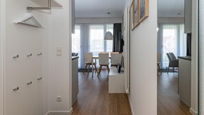 A modern hotel room with a wooden floor, a dining area with a table and chairs, and a view of the city through large windows. - Strandnahes Ferienapartment mit Balkon, Parkplatz, Schwimmbad- & Saunanutzung (Nordseeheilbad Bensersiel)