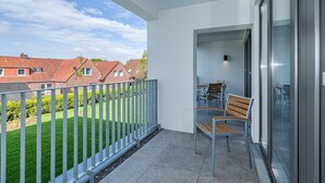 A balcony with a view of houses, a table with chairs, and a glass door. - Strandnahes Ferienapartment mit Balkon, Parkplatz, Schwimmbad- & Saunanutzung (Nordseeheilbad Bensersiel)