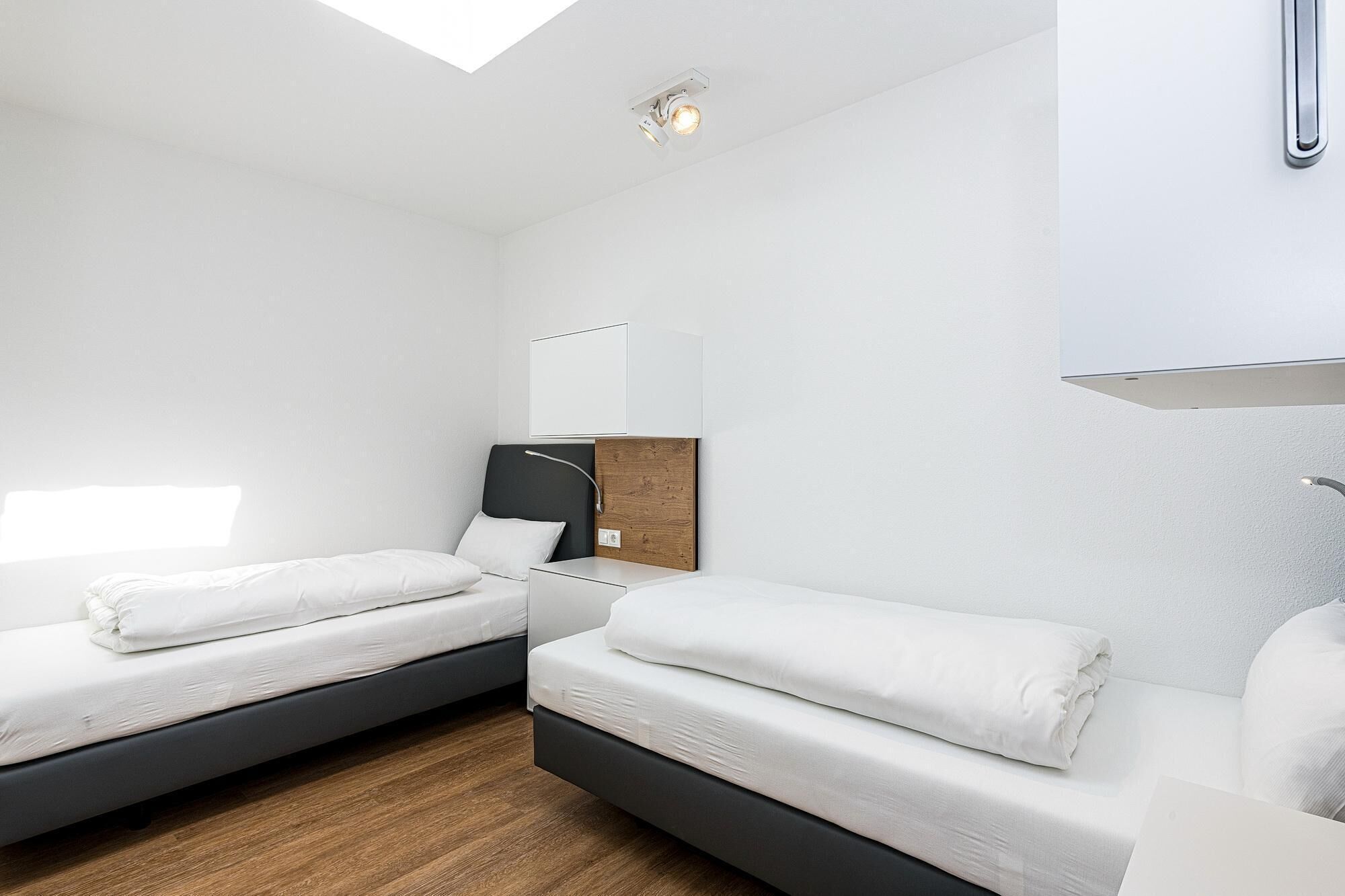 A modern hotel room with two single beds, a wooden floor, a large mirror, and a skylight.