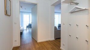 A hallway with wooden flooring, white walls, and a door leading to a room with a bed and a chair.