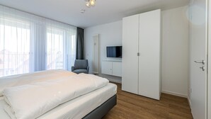 A modern bedroom with a large bed, a TV, a wardrobe, and a chair.