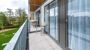Un balcon moderne agrémenté d’une pergola en bois, d’une table avec des chaises et de grandes portes-fenêtres coulissantes.