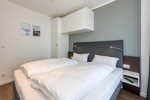 A modern hotel room with a large bed, a bedside table, a wardrobe, and two framed pictures on the wall. - Strandnahes Apartment mit Großem Balkon, Parkplatz, Schwimmbad- & Saunanutzung (Nordseeheilbad Bensersiel)