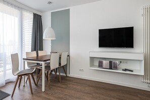 A modern hotel room with a dining area, a flat-screen TV mounted on a wall, and a built-in entertainment unit. - Strandnahes Apartment mit Großem Balkon, Parkplatz, Schwimmbad- & Saunanutzung (Nordseeheilbad Bensersiel)