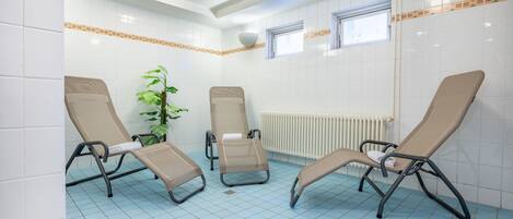 Ein Zimmer mit drei Liegesesseln, einer Topfpflanze und einem Fenster.
