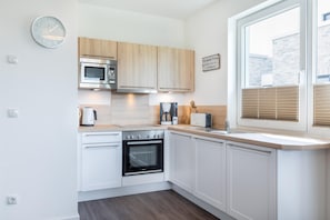 A modern kitchen with white cabinets, a built-in oven, a microwave, a coffee maker, and a toaster.