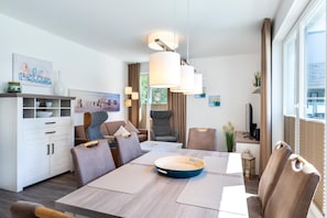Un comedor moderno y bien iluminado con una mesa de madera, sillas acolchadas y un centro de mesa con un tazón azul.