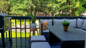 Una terraza exterior con una parrilla, una zona de estar y vistas a un jardín.