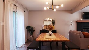 Un comedor con una mesa de madera, bancos, un jarrón con flores secas, una planta en maceta y una lámpara de araña moderna.