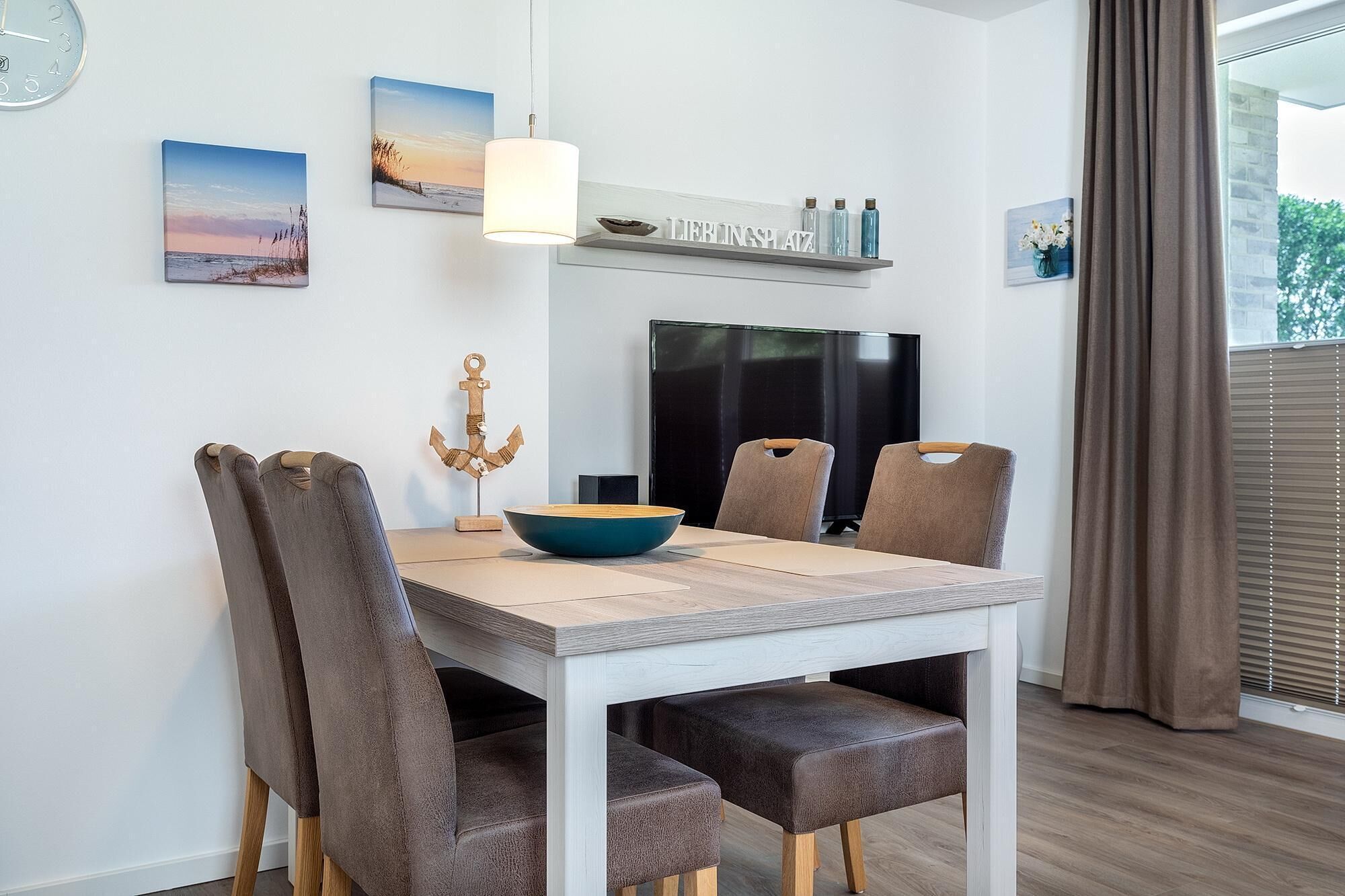 Un comedor con una mesa, sillas, un cuenco, una lámpara colgante y obras de arte en la pared.