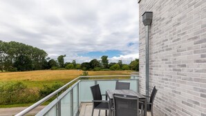 A balcony with a table and chairs, overlooking a grassy field and trees.