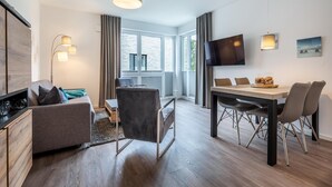 A modern hotel room with a dining area, a sofa, a TV, and a large window.