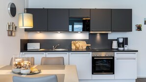 A modern kitchen with dark cabinetry, a built-in oven, a coffee maker, and a wooden cutting board.
