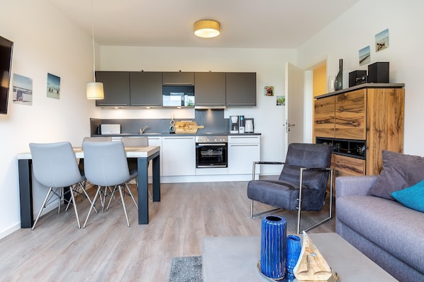 A compact living space with a kitchenette, a dining area with chairs, a sofa, and a coffee machine.