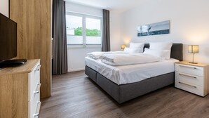 A modern hotel room with a large bed, bedside tables, a flat-screen TV, and a window with curtains. - Strandnahes Familienapartment mit Toller, Sonniger Dachterrasse und Zwei Bädern (Ostseebad Boltenhagen)