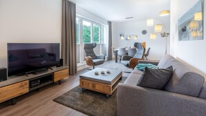 A modern living room with a flat-screen TV, a wooden coffee table, a grey sofa, and a dining area with chairs and a table. - Strandnahes Familienapartment mit Toller, Sonniger Dachterrasse und Zwei Bädern (Ostseebad Boltenhagen)