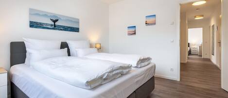Et hotelværelse med en stor seng, et natbord, et skrivebord og en skrivebordslampe. Der er tre billeder på væggen og en dør, der fører til et andet rum.