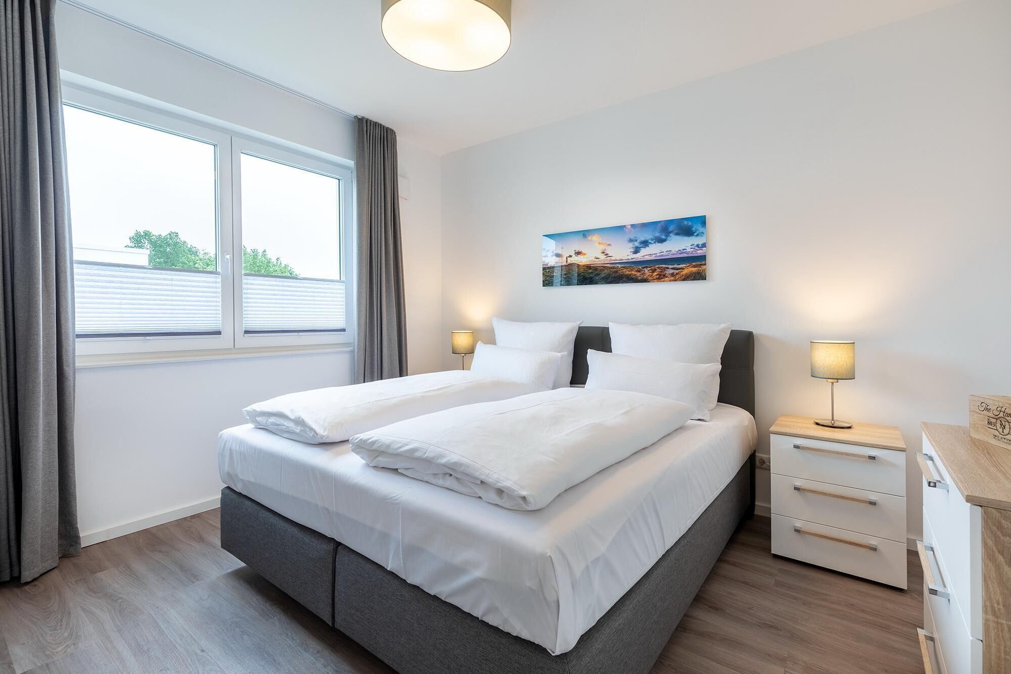 A modern hotel room with a large bed, two bedside tables, a nightstand, and a painting on the wall.