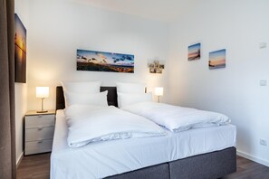 A modern hotel room with a large bed, two bedside tables, and wall-mounted artwork. - Liebevoll Eingerichtetes Apartment mit Tollem, Sonnigem Balkon in Strandnähe (Ostseebad Boltenhagen)