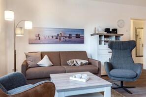 A living room with a sofa, two armchairs, a coffee table, and a painting of a beach scene.
