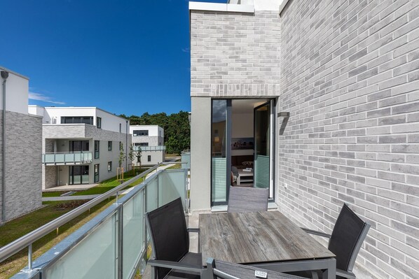 A modern balcony with a table and chairs, overlooking a residential area with similar buildings.