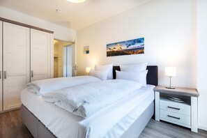 A modern bedroom with a large bed, bedside tables, a nightstand, and a painting on the wall.