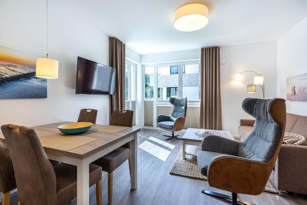A modern living room with a flat-screen TV, a dining table with chairs, and a sofa.