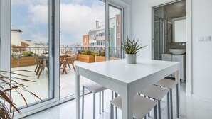 Eine moderne Küche mit einem großen Fenster, einem Essbereich mit weißem Tisch und Stühlen sowie einer Topfpflanze auf dem Tisch.