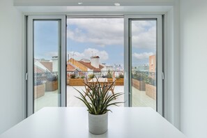 A balcony with a potted plant, a table, and a view of the cityscape through open sliding doors.