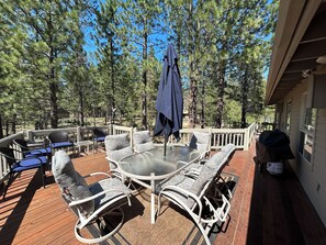 Eine Terrass mit rundem Tisch und Stühlen, umgeben von einem Holzdeck und einem weißen Geländer.