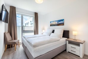 Una habitación de hotel con cama, mesitas de noche, una silla, televisor y ventana con cortinas.