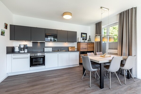 Una cocina moderna con armarios blancos y gris oscuro, un horno empotrado y una zona de comedor con mesa y sillas.