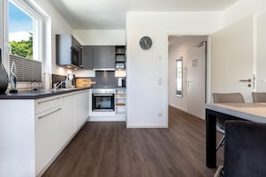 Una cocina moderna con horno integrado, una zona de comedor con mesa y sillas, y un reloj en la pared.