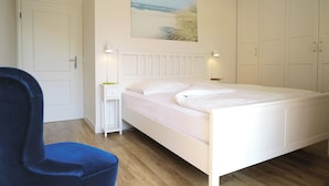 Ein Schlafzimmer mit Bett, Stuhl, Nachttisch, einem Wandbild und einem Kleiderschrank.