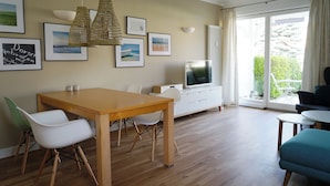 Ein modernes Wohnzimmer mit einem Holzesstisch, weißen Stühlen, einem Fernseher und einem Sofa.