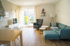 A modern living room with a sofa, armchair, and a dining area with a table and chairs.