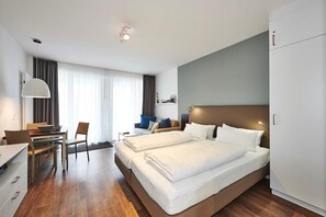 A modern hotel room with a large bed, a desk with a chair, a dining table, and a sofa.