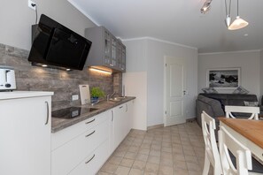 Una cocina moderna con una televisión de pantalla plana, armarios blancos, un salpicadero de madera y una zona de comedor con mesa y sillas de madera.