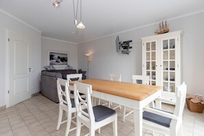 Un comedor con una mesa de madera y sillas blancas, un sofá gris y un aparador con puertas de cristal.