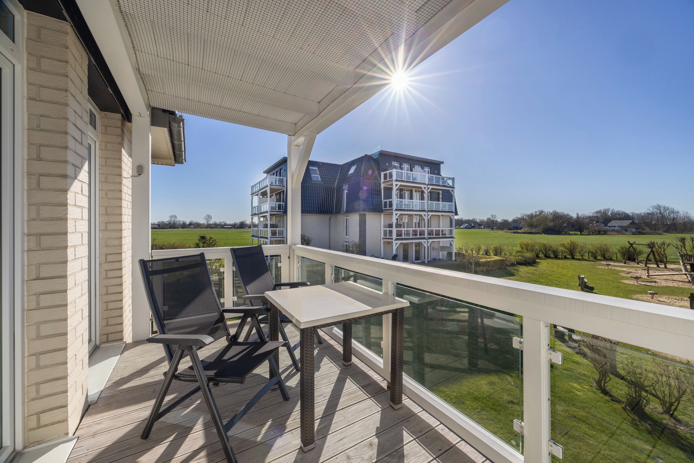 A balcony with a table and chairs, overlooking a residential area with houses and a clear sky.