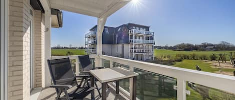 A balcony with a table and chairs, overlooking a residential area with houses and a clear sky.