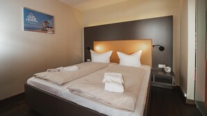 Habitación de hotel con una cama grande, dos mesitas de noche y una lámpara de pared.