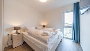 Una habitación de hotel moderna con una cama grande, lámparas de noche, una mesita de noche y vistas de la ciudad a través de un ventanal amplio.