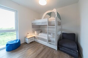 Un lit superposé avec un bureau et une chaise, une fenêtre donnant sur un paysage verdoyant et un fauteuil en forme de poire de couleur bleue.