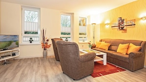 Una sala de estar con un sofá marrón, un sillón marrón, una mesa de centro y un televisor sobre un mueble.